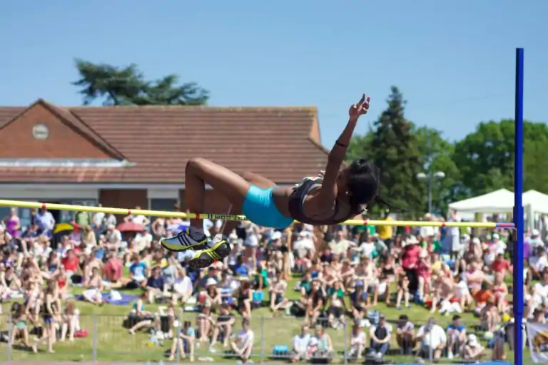 a woman jumping over a high jump in front of a crowd